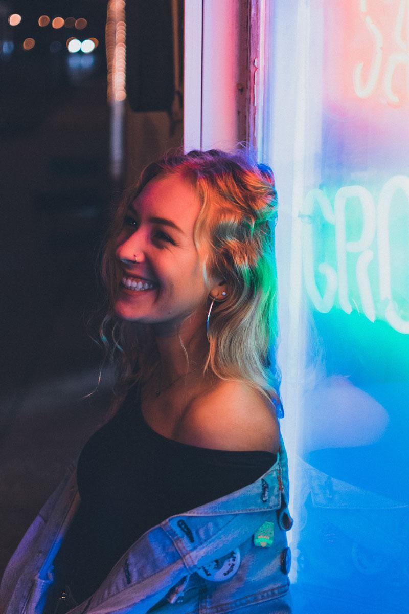 girl smiling in front of neon sign illustration for quotes about happiness and smiling